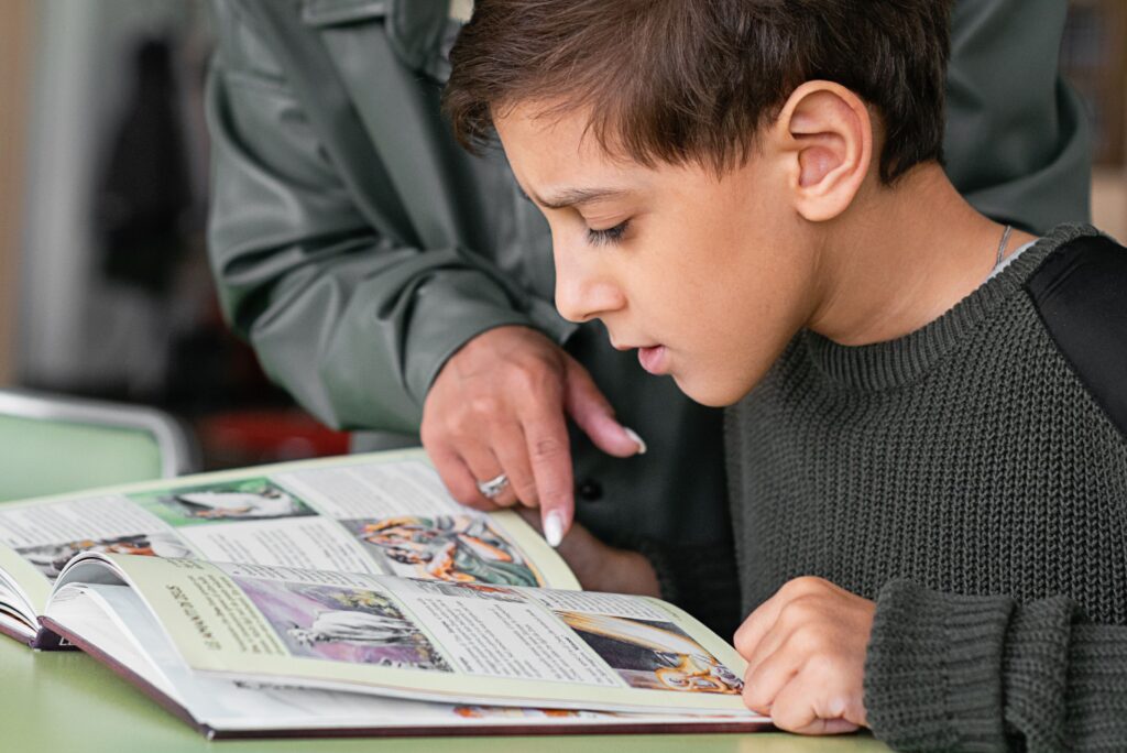 Boy concentrating on reading as adult points out text in a book.